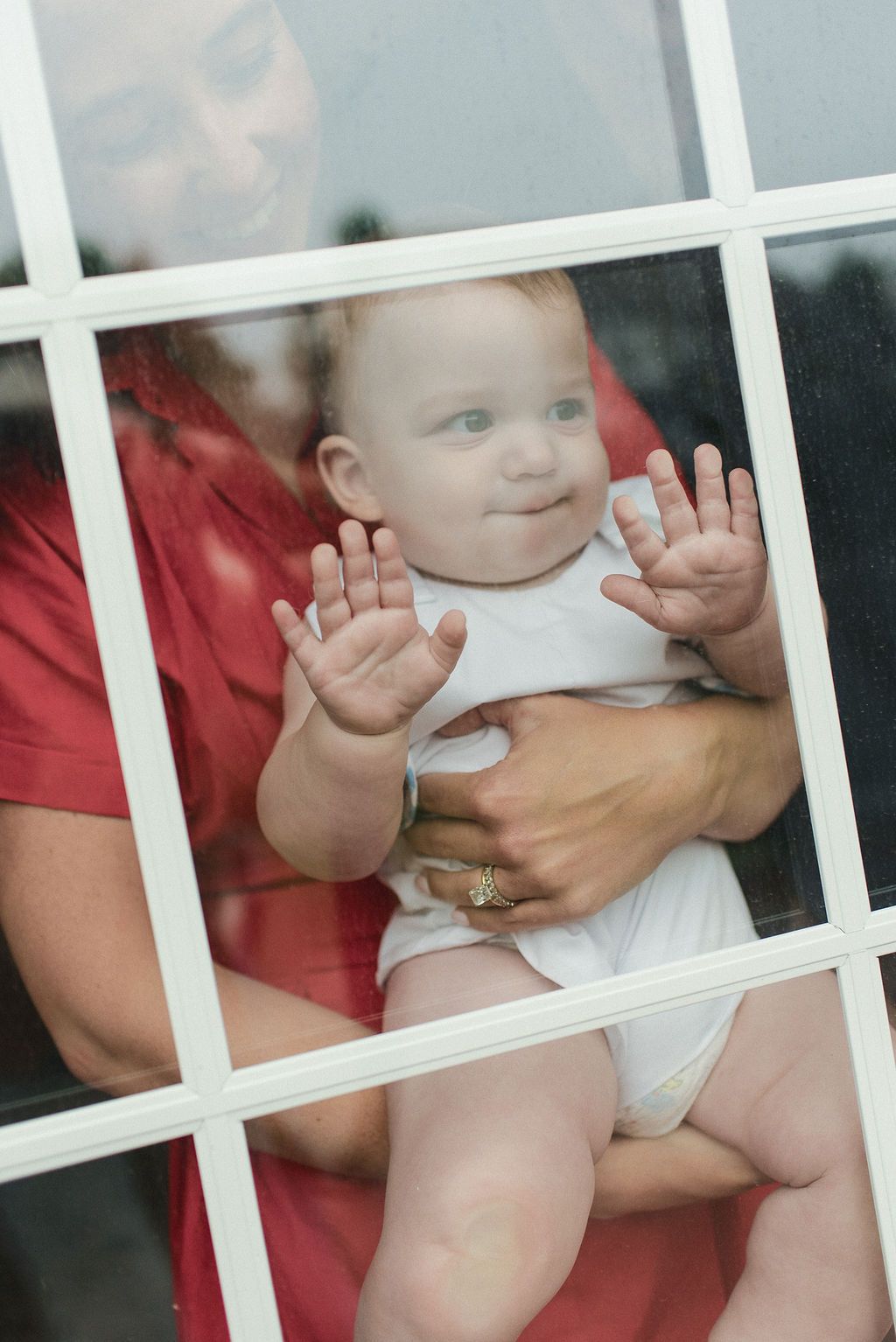 Baby in a white diaper reaches through white vertical bars with playful enthusiasm.