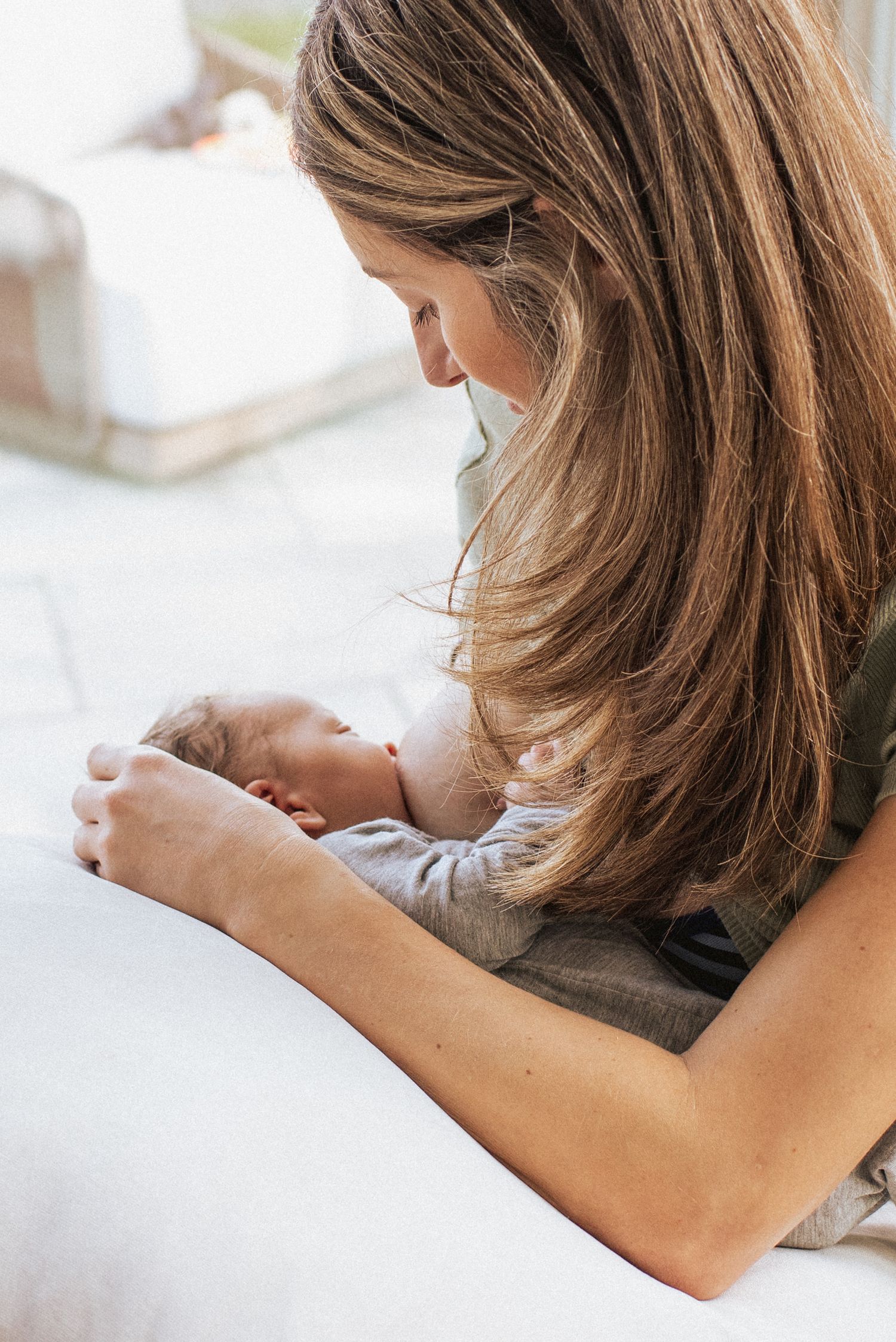 A tender moment between parent and newborn as they cuddle together on white bedding while laying down.