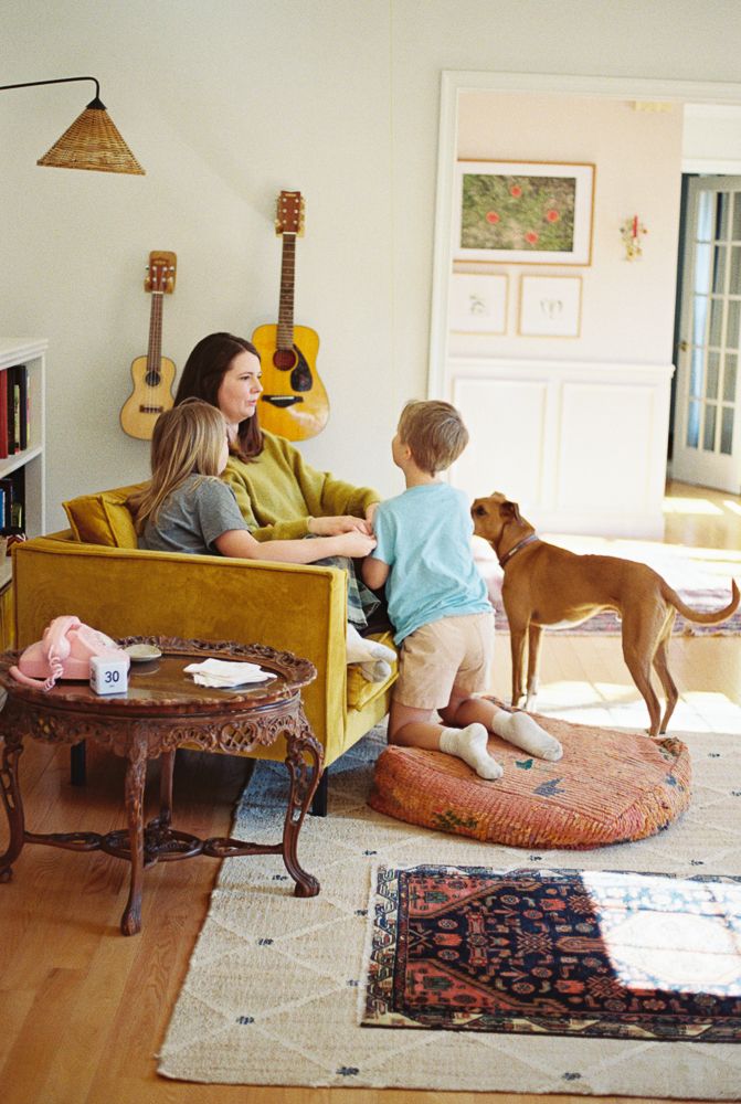 Dog lounges on an ornate ottoman in a bright living room while people gather on nearby furniture.