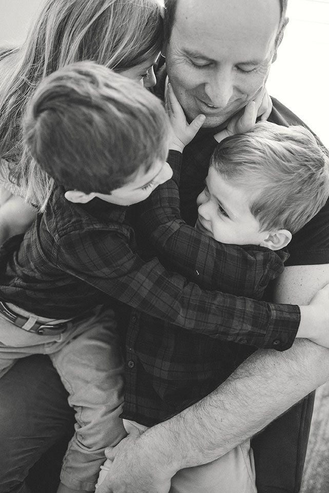 Black and white candid portrait of loving family embrace and playful moment between parent and children outdoors.