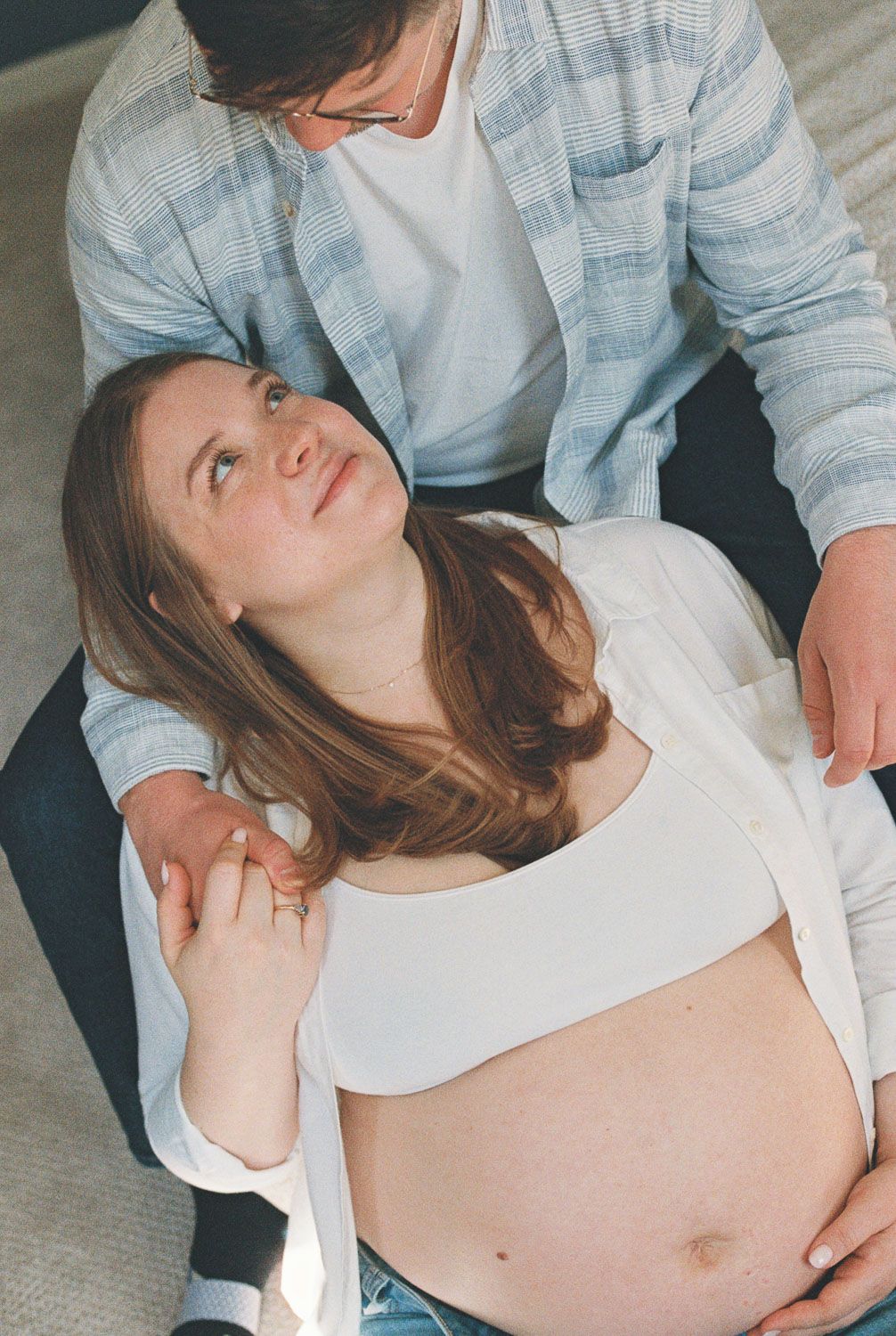 Pregnant woman in white crop top looks up lovingly at partner during an intimate maternity photo session.