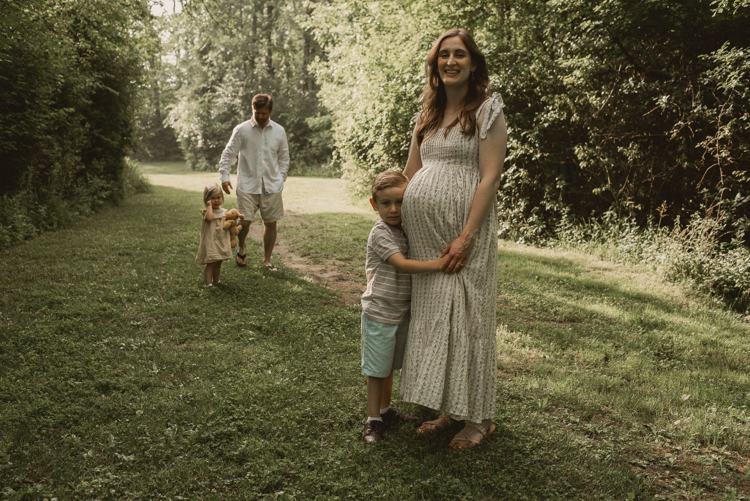 An intimate outdoor family photo session captured on a sunny afternoon in a lush green park setting.