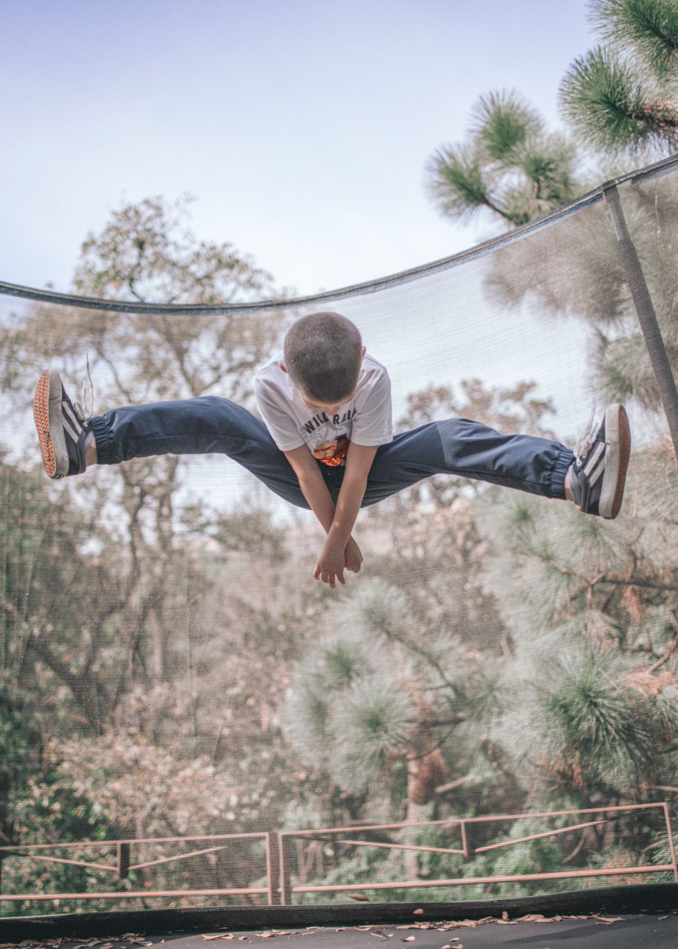 Person in athletic pose performing a dramatic split jump across a forest path with pine trees in the background.