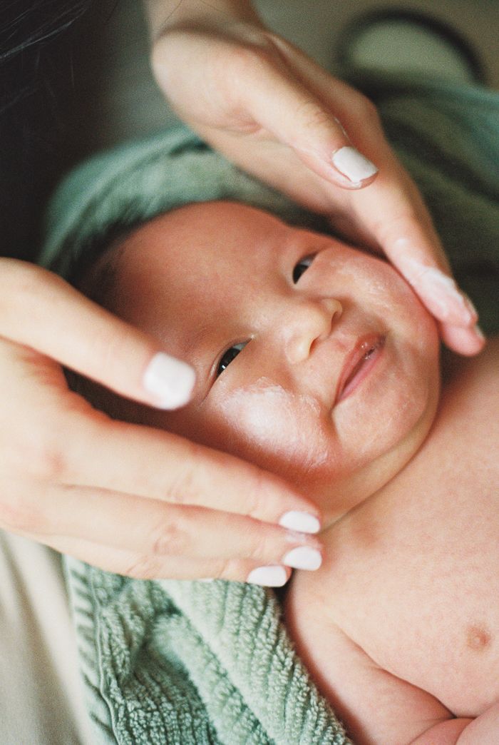 A newborn baby wrapped in a green blanket being gently cradled by a mother's hands with white manicured nails.