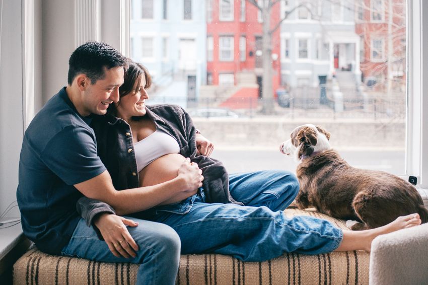 A couple sits together on a couch by a window in a cozy living room setting.