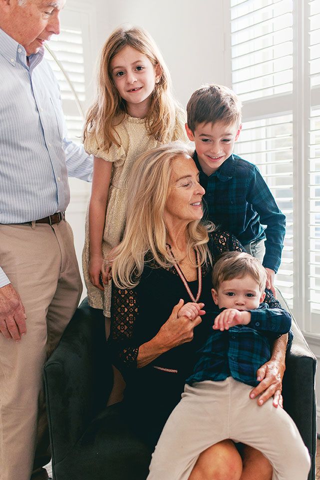 A family poses together by a window, dressed in coordinating casual outfits in blue and neutral tones.