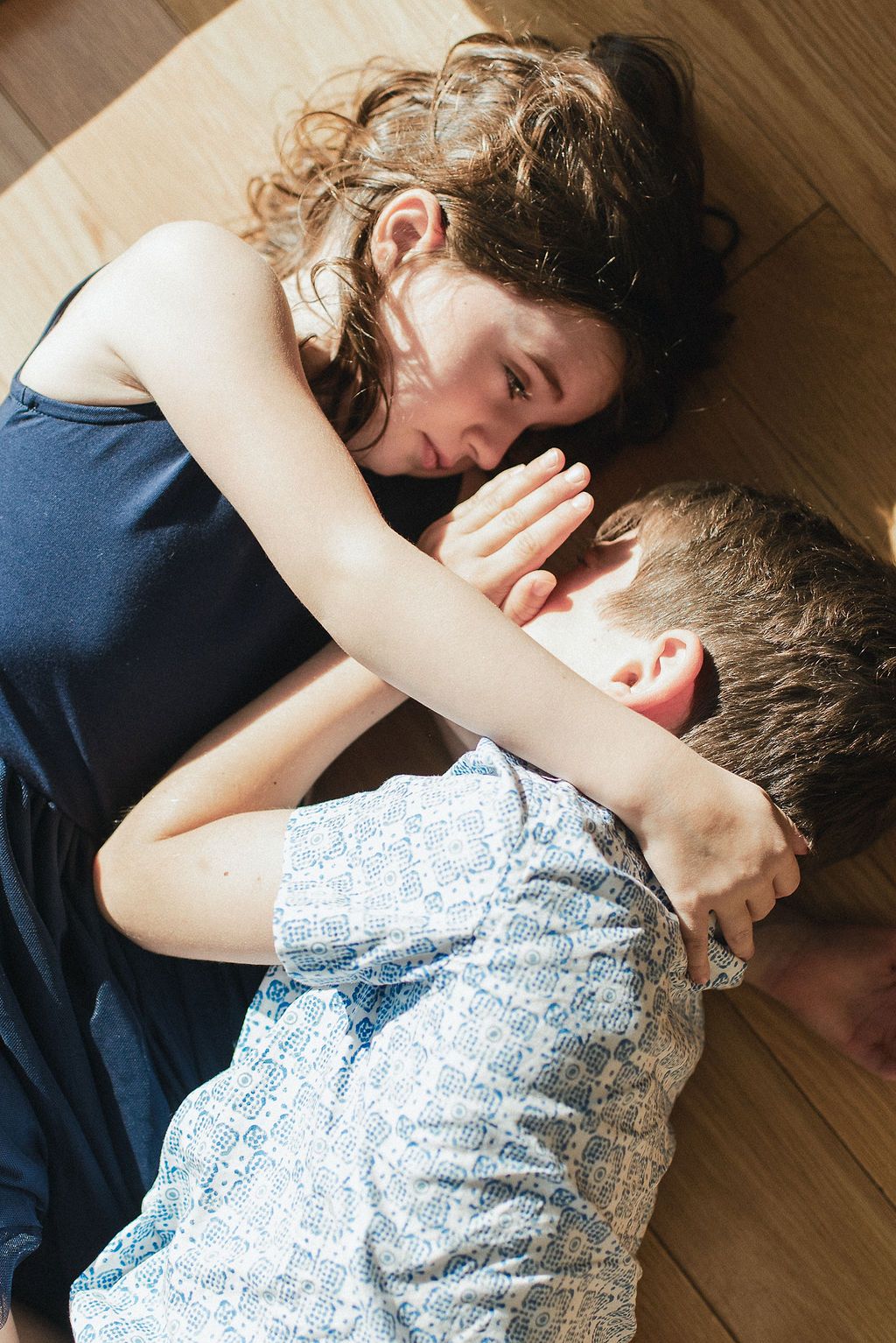 Two people lying close together on a wooden floor in an intimate moment of connection and comfort.