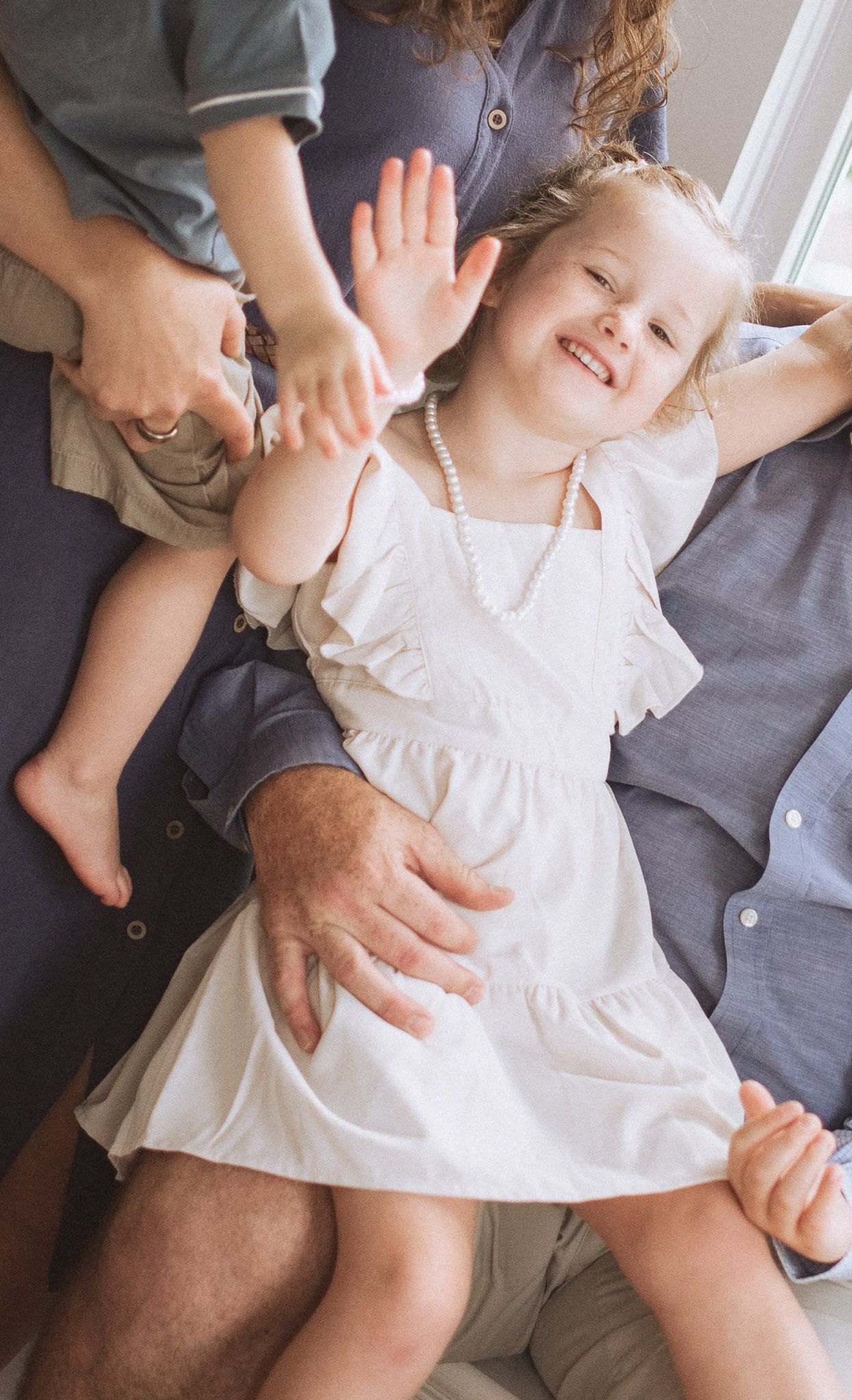 A series of candid moments showing a child in a white dress laying on a grey couch.