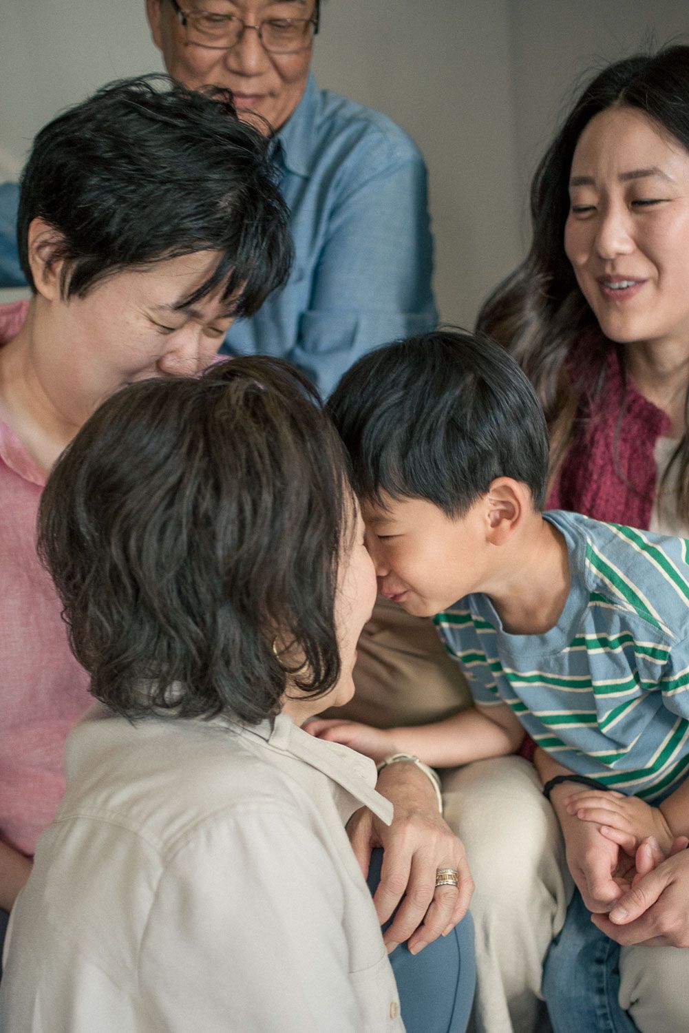 Multigenerational Asian family sharing a warm moment together, with young boy leaning in close to elderly woman.