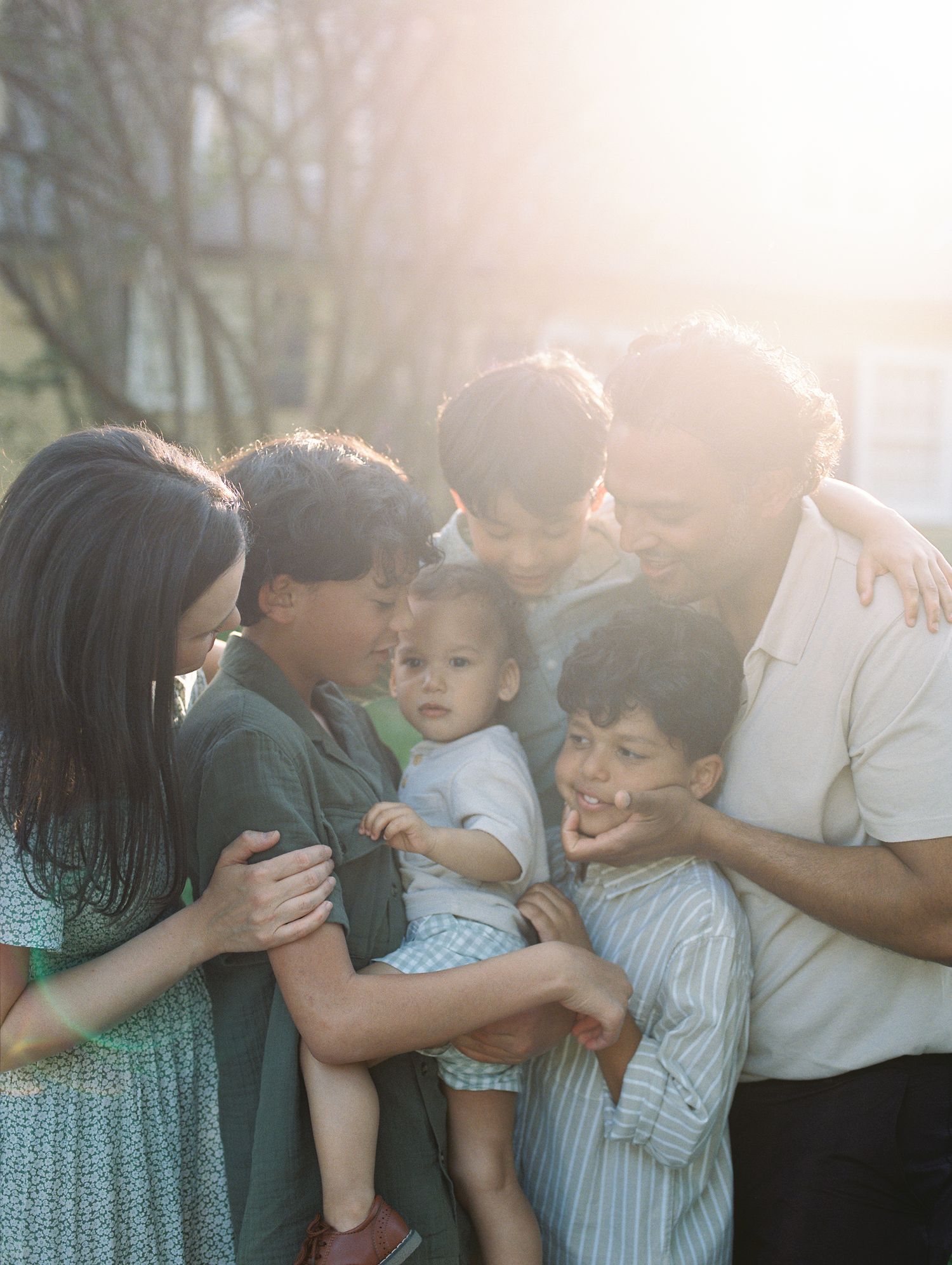 Family sharing joyful laughter and hugs together outdoors in warm sunlight.