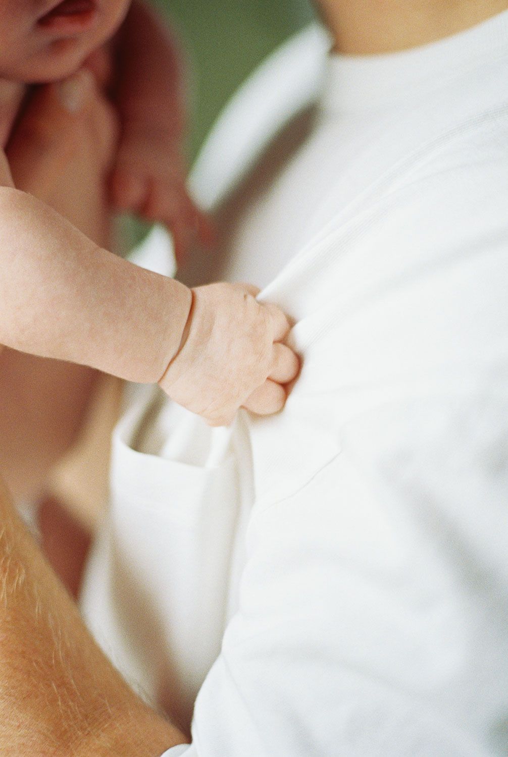 A tiny newborn baby hand grasping an adult's white shirt, symbolizing the bond between parent and child.