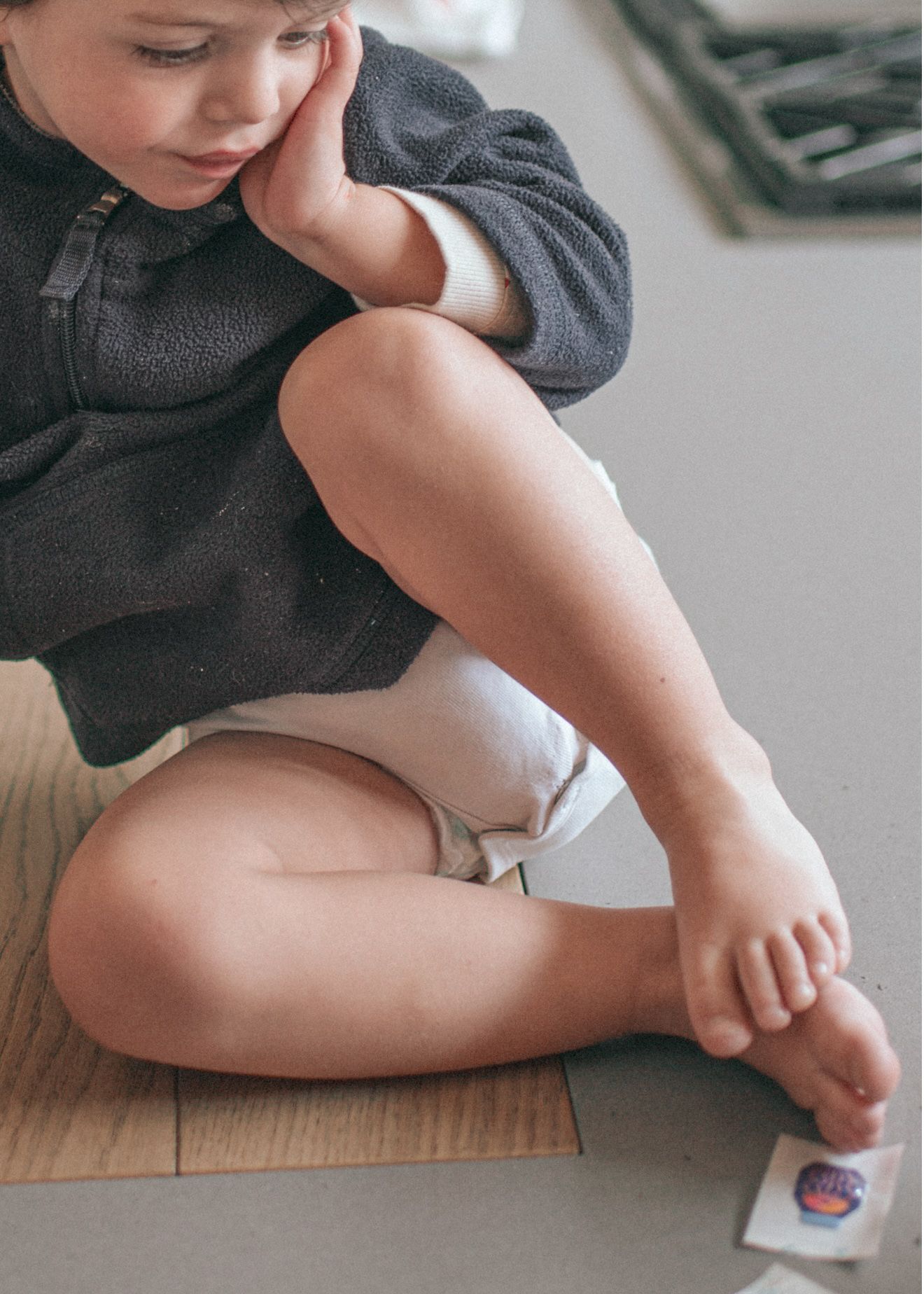 Close-up view of small legs and feet resting on hardwood floor with a light colored sock being pulled on.