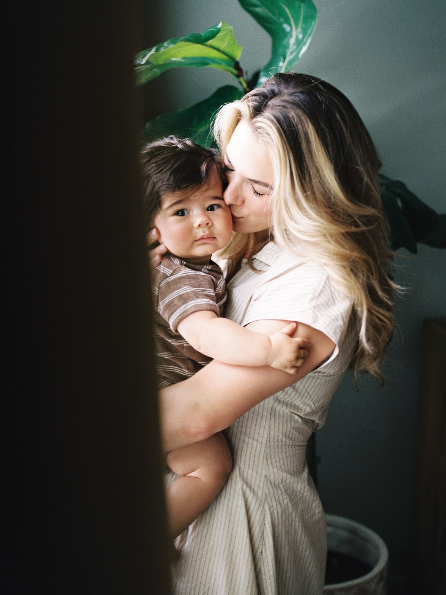 A tender moment captured in moody lighting with green foliage, showcasing an intimate embrace against a dark background.