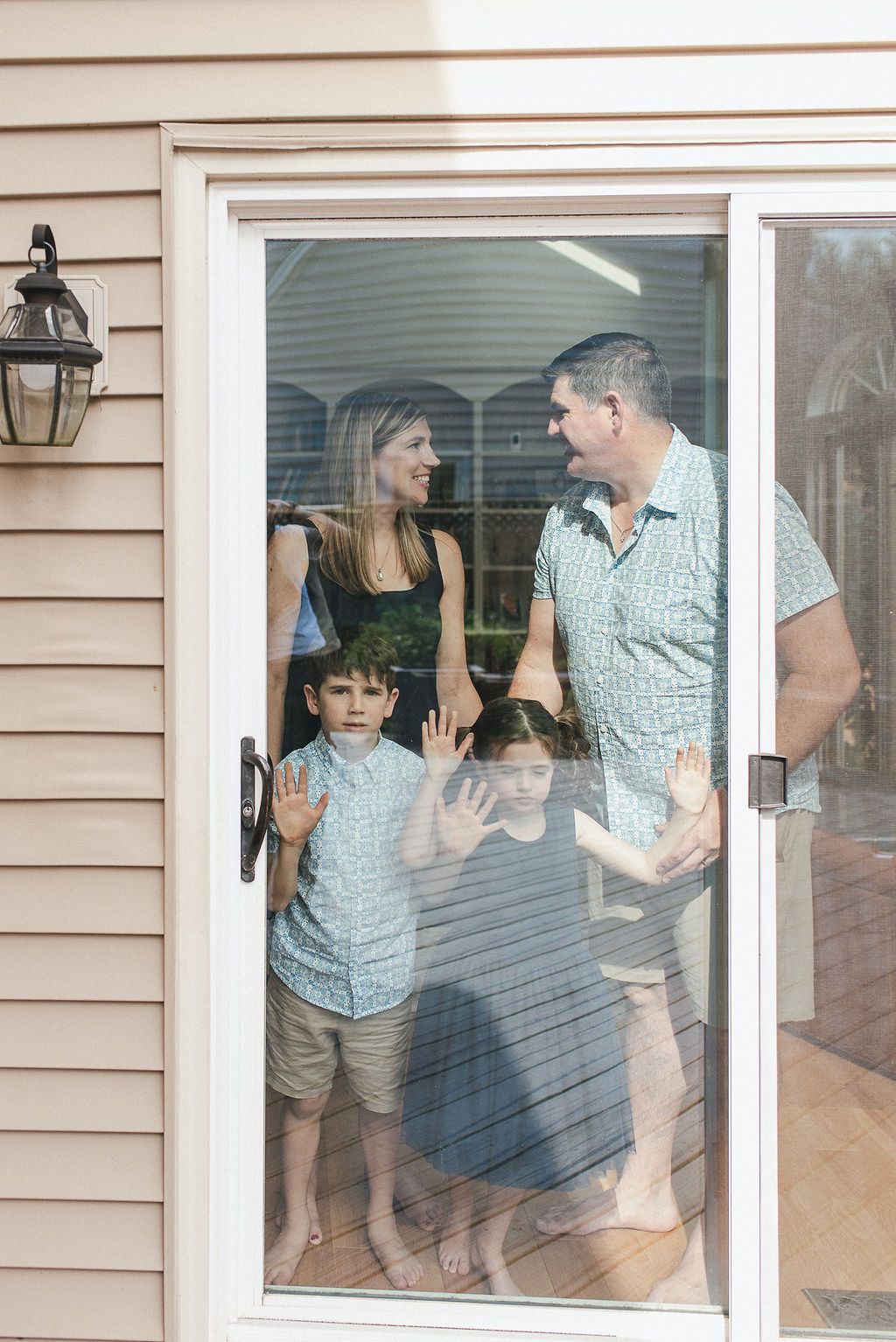 Family members playfully press hands against window panes of house exterior.