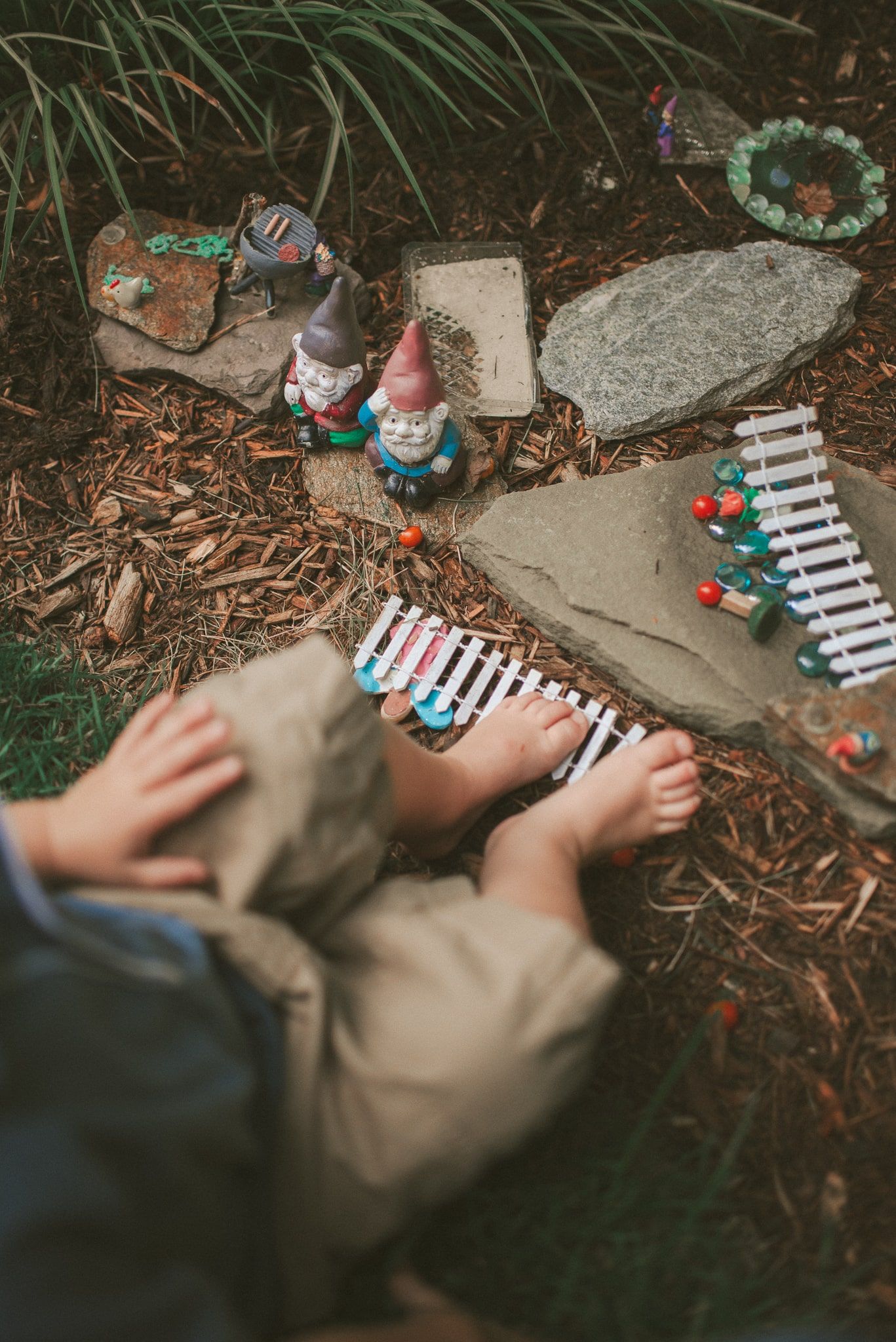 A sequence of hands playing with small toys and objects on a natural outdoor surface.