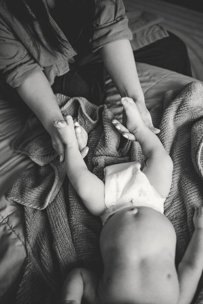 Black and white photo of a mother changing her baby's diaper on a soft blanket on a bed.