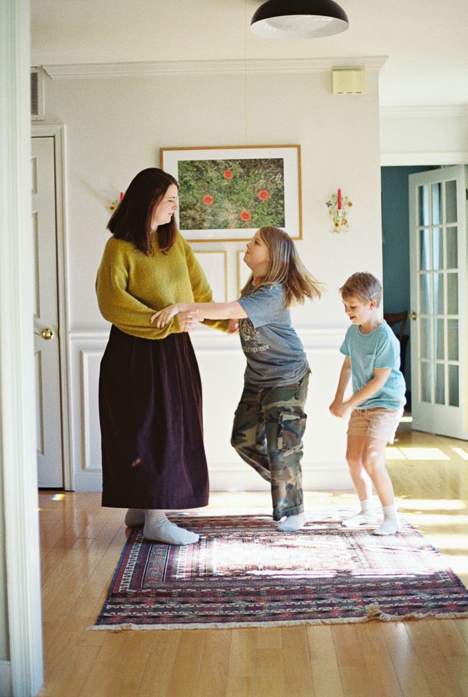 A sequence of people playing and dancing on a decorative rug in a sunlit hallway.