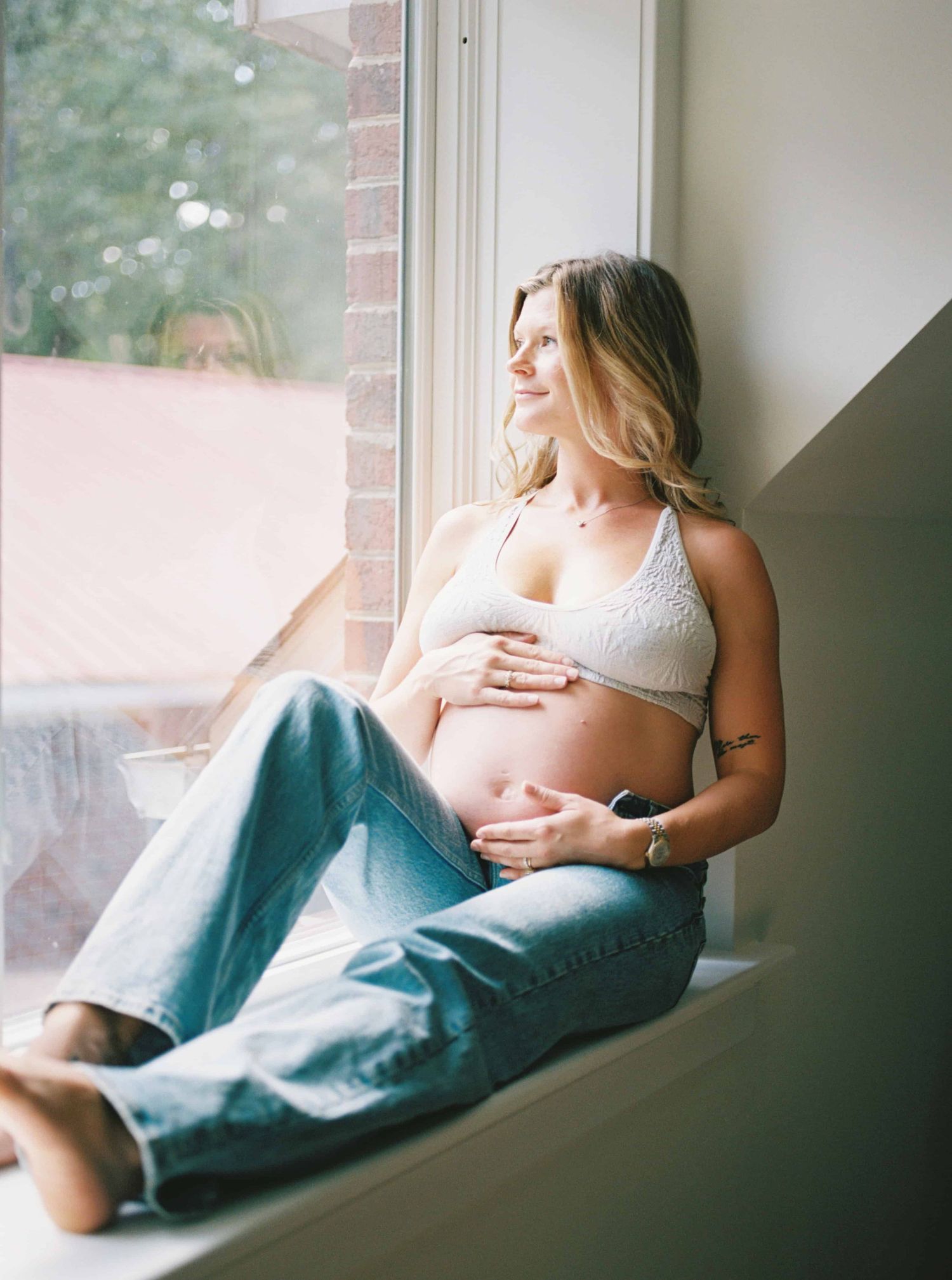 Person resting on window sill in casual clothing with natural light streaming in.