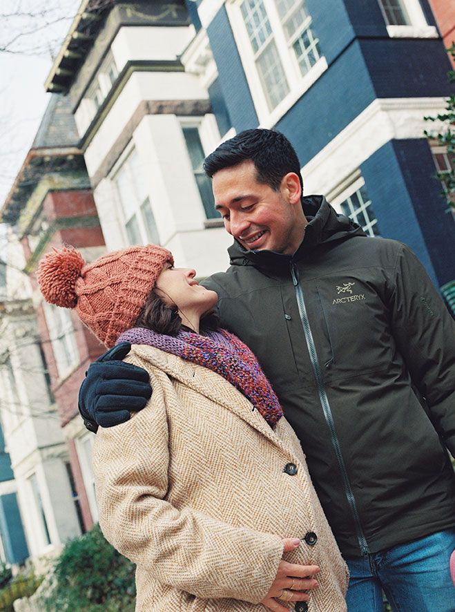 Couple sharing a playful moment together outdoors in front of a white building facade.
