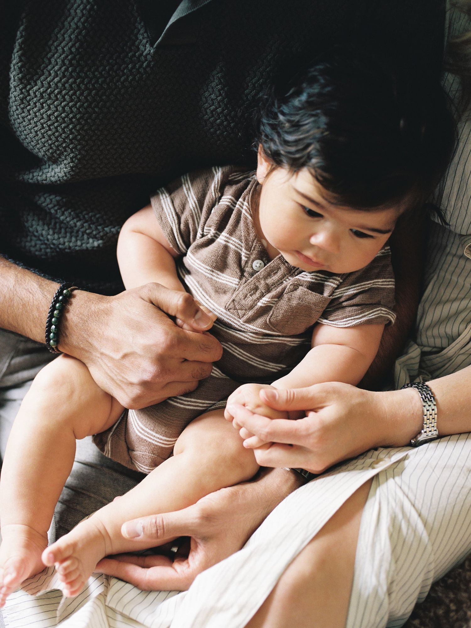 A young toddler in beige clothing receiving care for a small wound on their leg with loving hands assisting them.