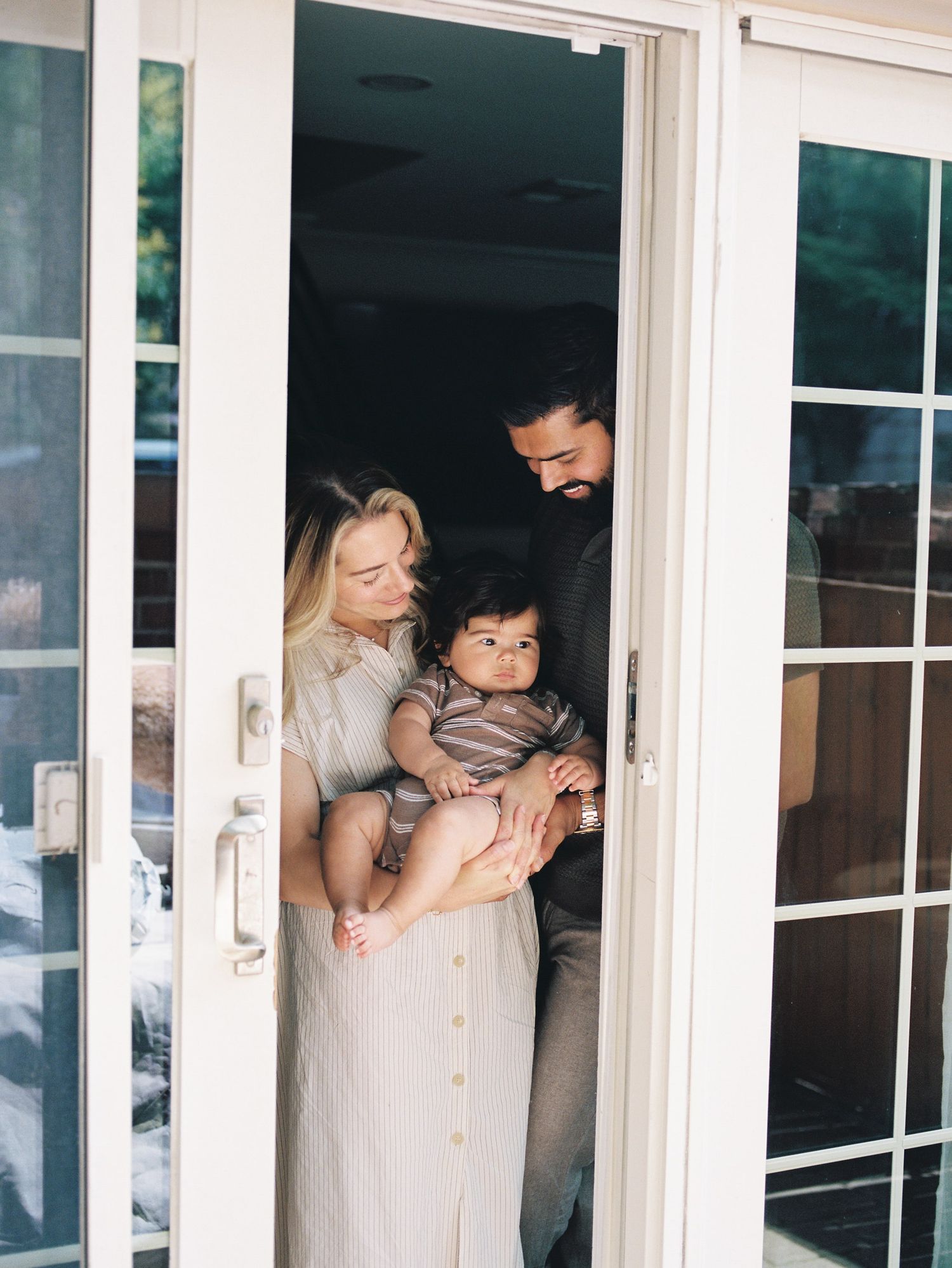 A loving family moment captured through glass French doors showing parents holding and playing with their young children.