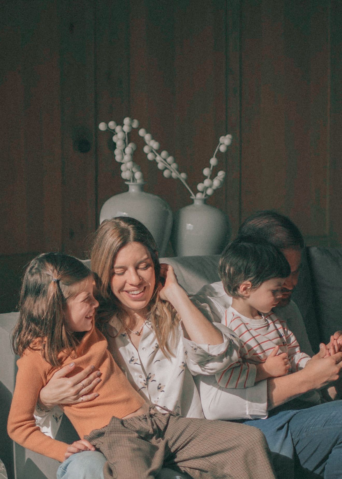 A family shares a cozy moment together on a dark sofa with decorative vases in the background.
