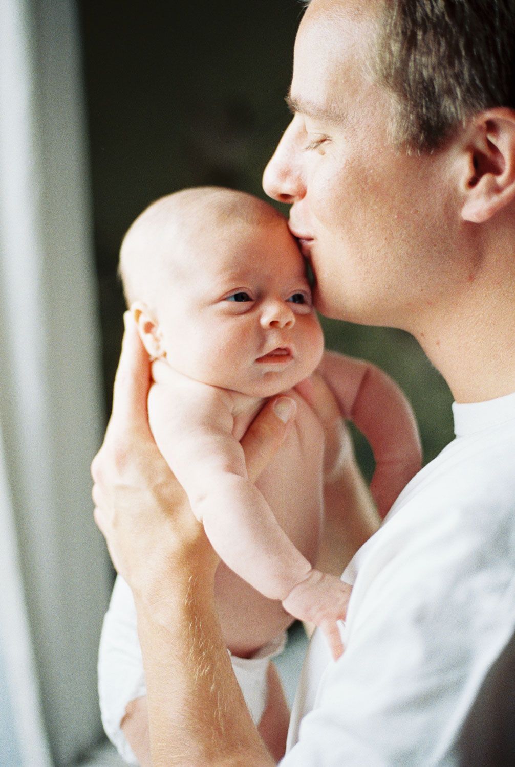 A loving father gently kisses his newborn baby on the head while carefully cradling the infant in his hands.