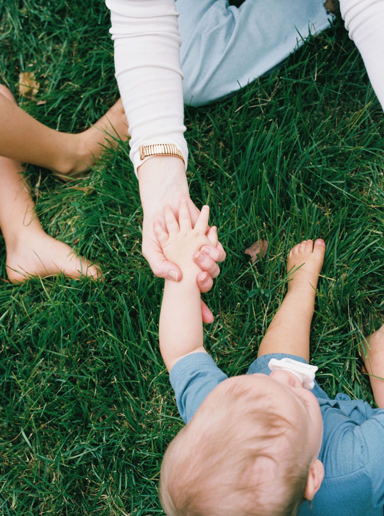 A sequence of images showing hands gently massaging a baby's legs on green grass outdoors.