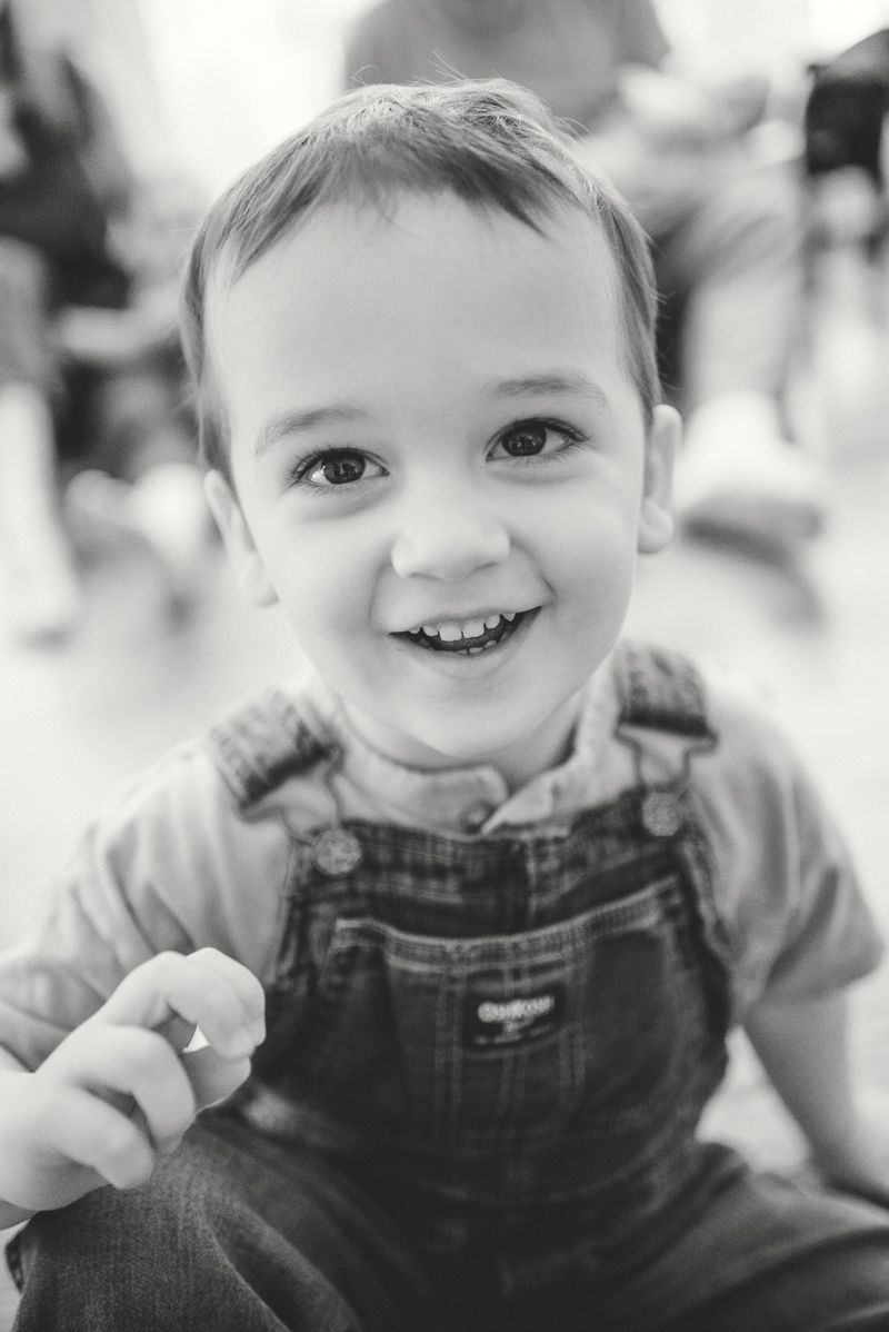 Black and white portrait of a smiling toddler boy wearing denim overalls, looking cheerfully at the camera.