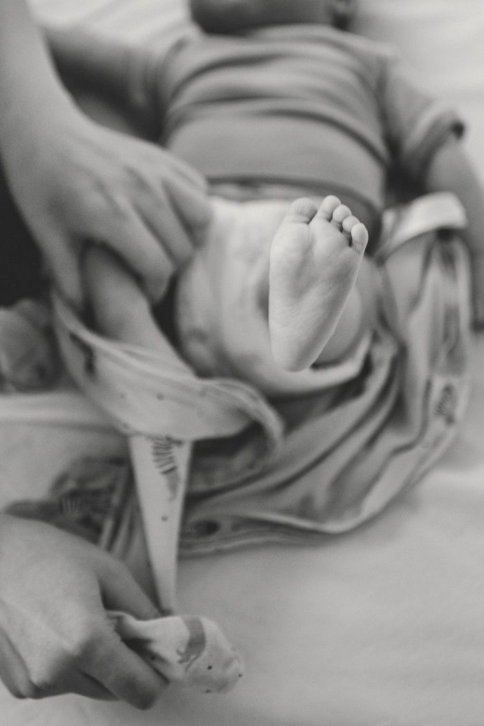 Black and white photo of newborn baby feet being held by parents hands after birth.