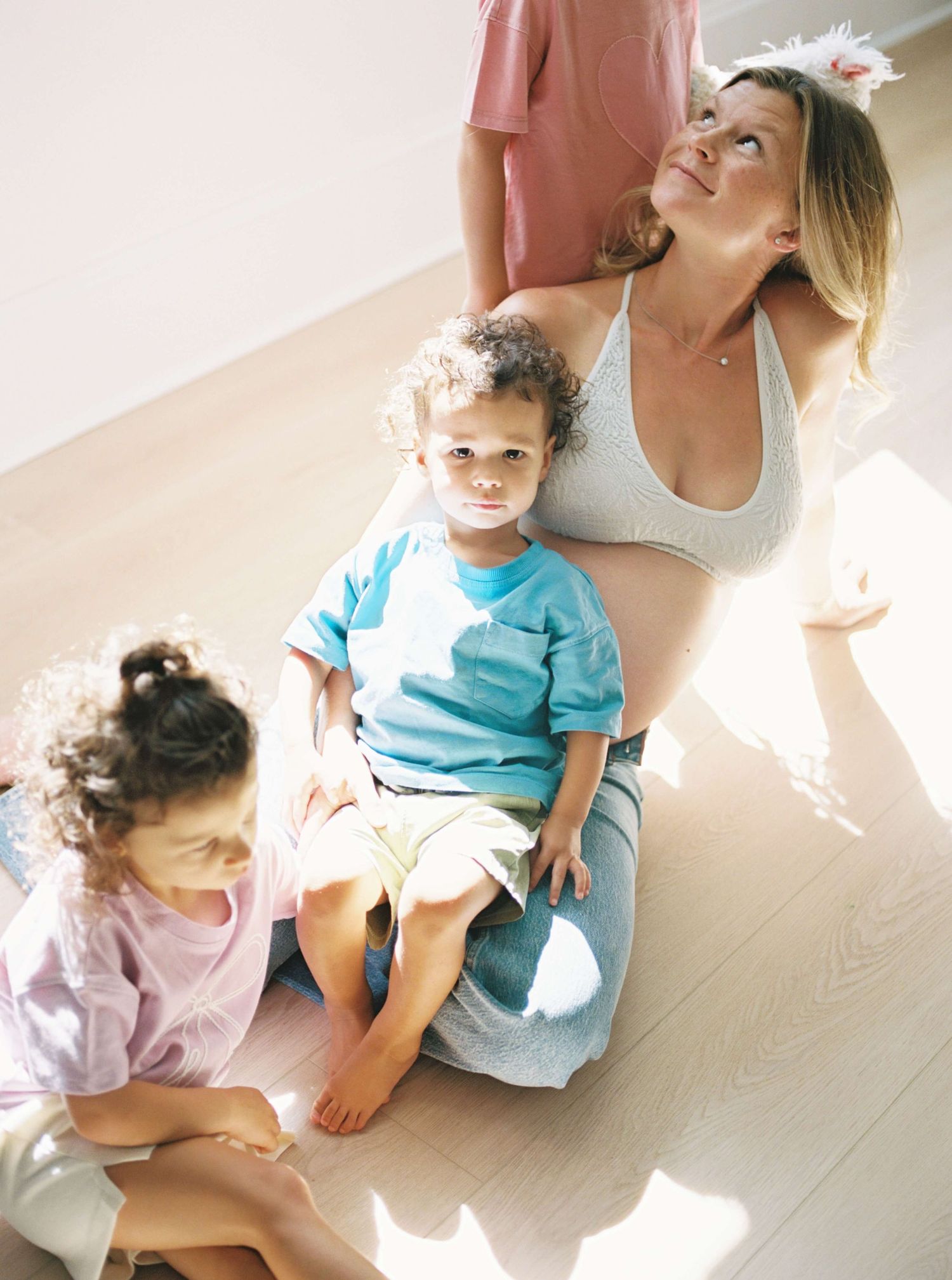 Family enjoying a playful moment together on the floor in sunlit room with children in casual attire.