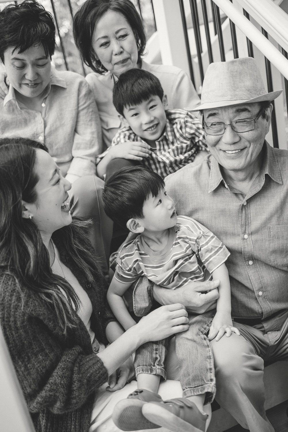 Black and white photo of a multigenerational Asian family smiling together on porch steps.