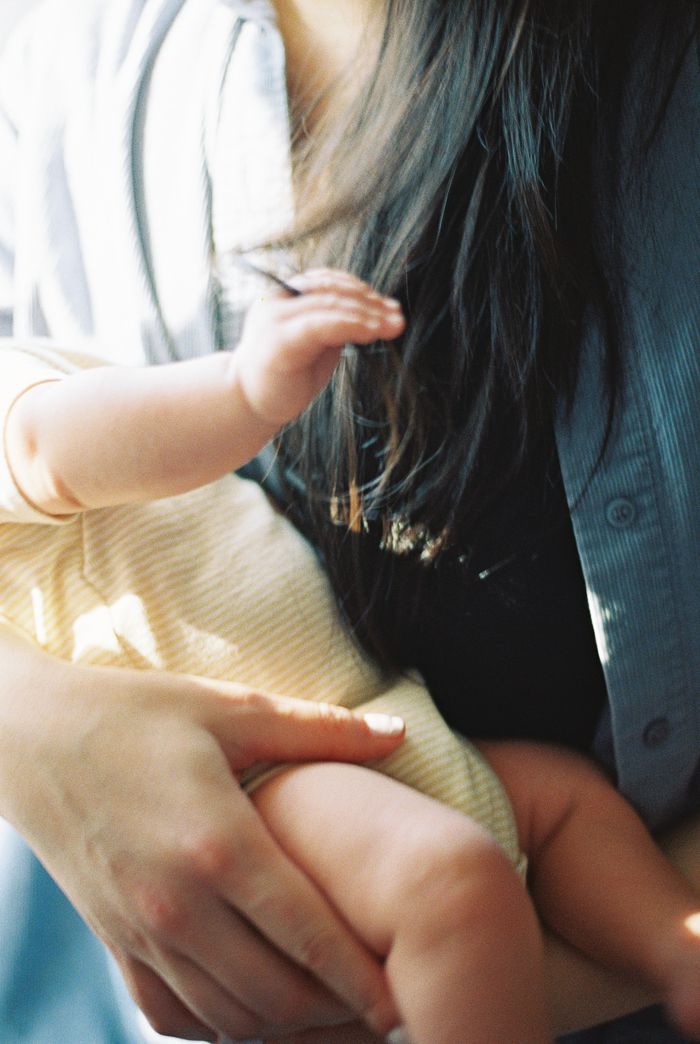 A baby's tiny hand grasping a mother's dark hair while being cradled in her arms.