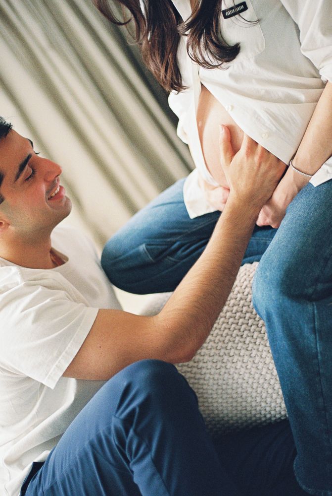 Person in white t-shirt and blue pants lying on couch showing signs of discomfort or pain.