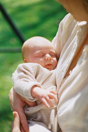 Newborn baby sleeping peacefully in mother's arms outdoors on a sunny day.