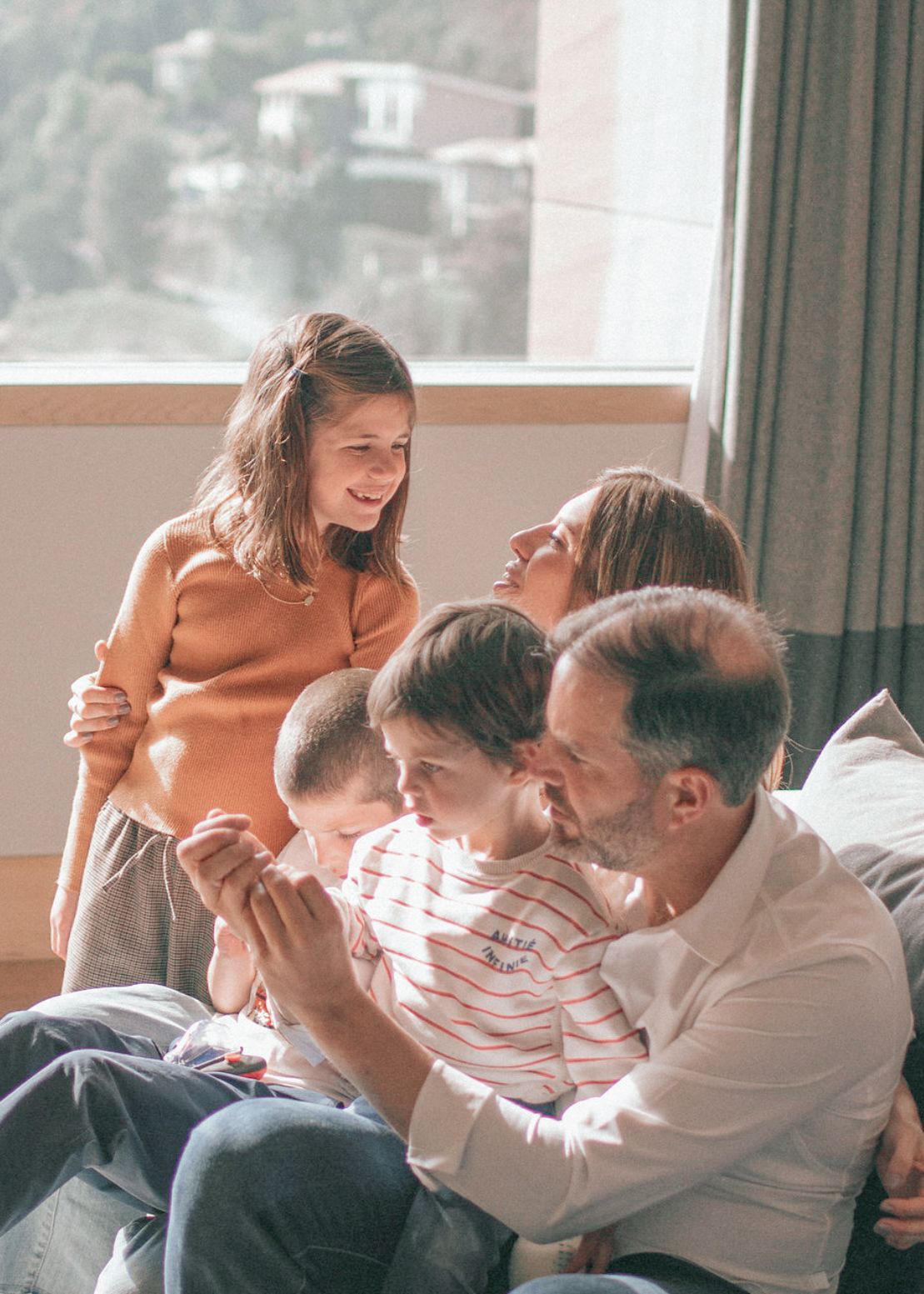 Multigenerational family members laughing together while sitting on a couch in bright sunlight.