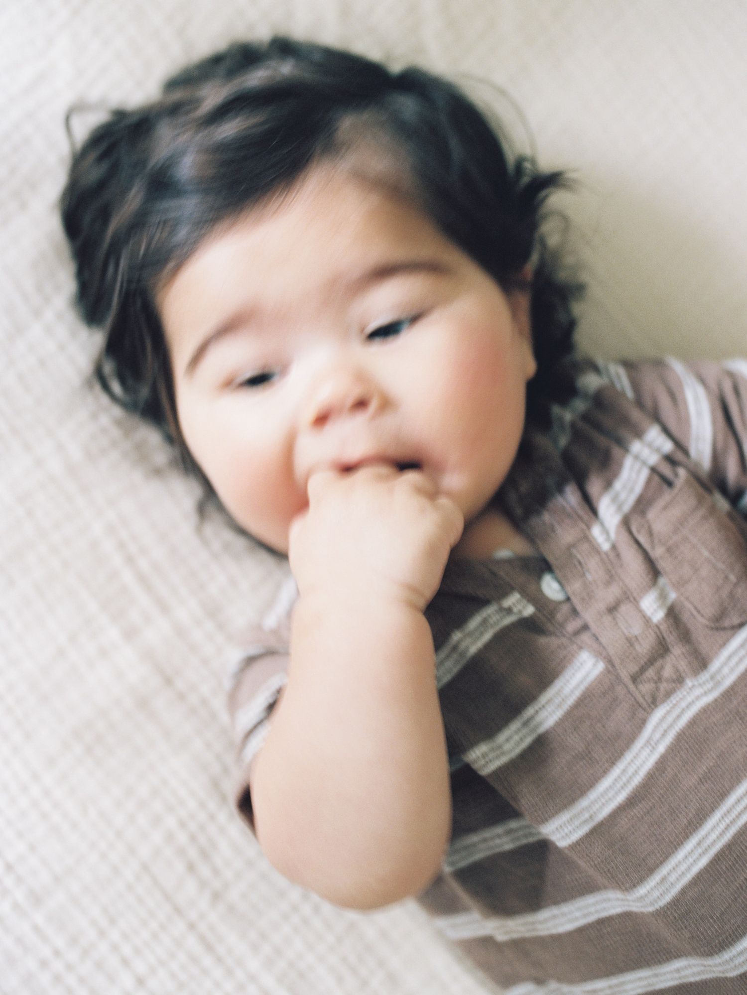 Side view progression photos show an infant with full dark hair in a brown outfit sucking their thumb while lying down.
