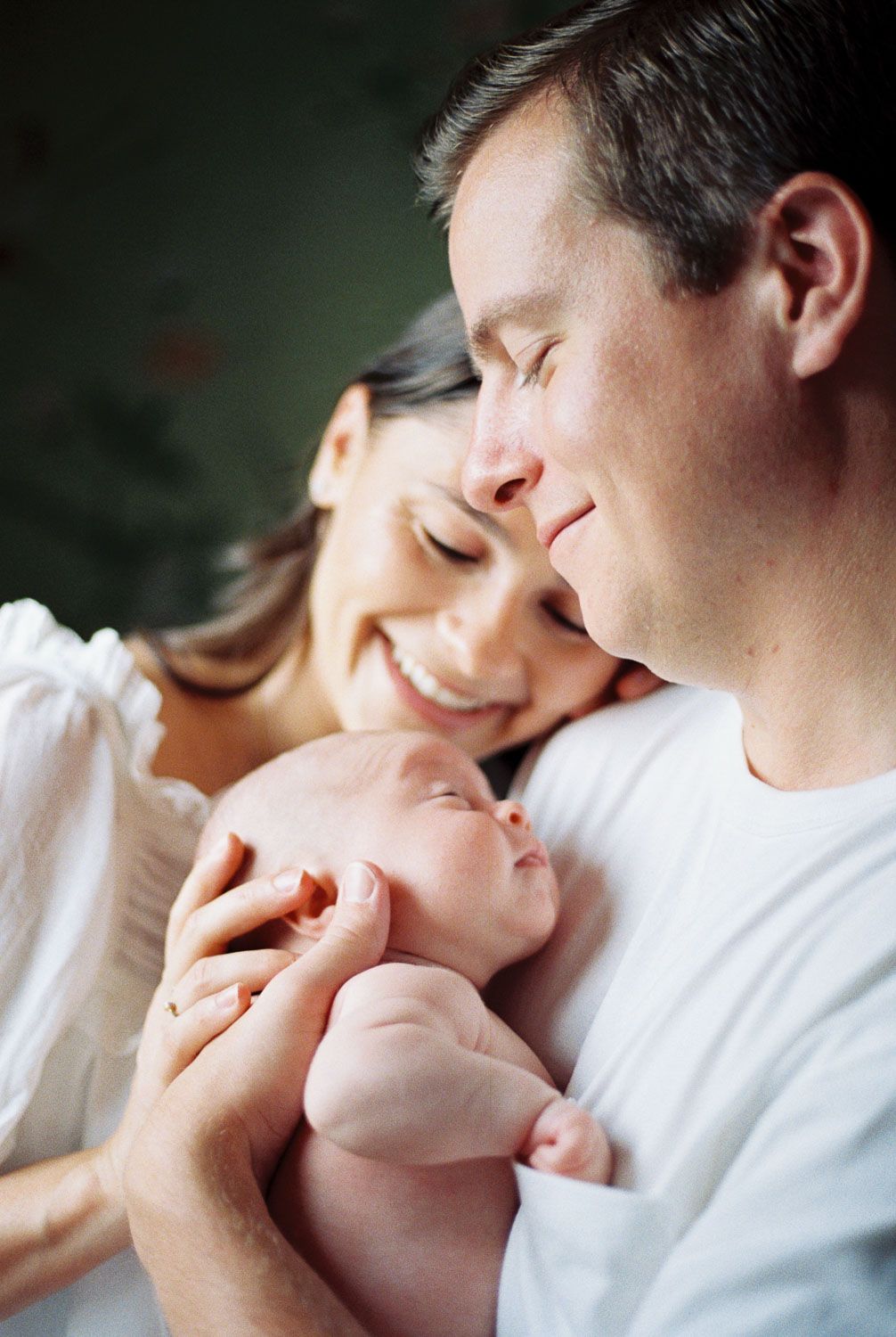 Happy parents smiling and cradling their sleeping newborn baby in a tender and loving family portrait.
