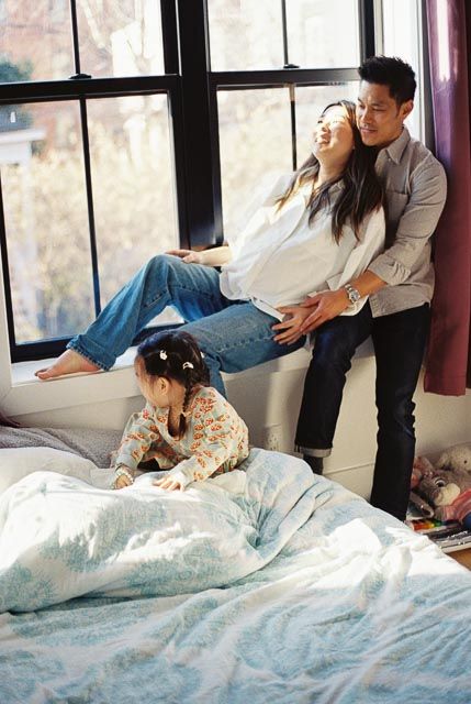 Happy Asian family with pregnant mother, father, and young daughter enjoying time together by bedroom window.