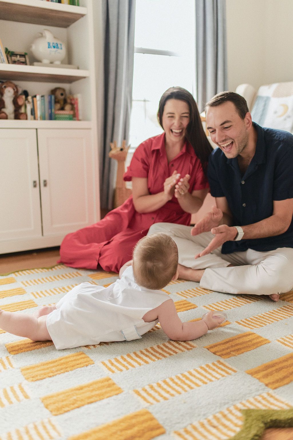 Family enjoying playtime with baby on geometric patterned rug in bright living room.