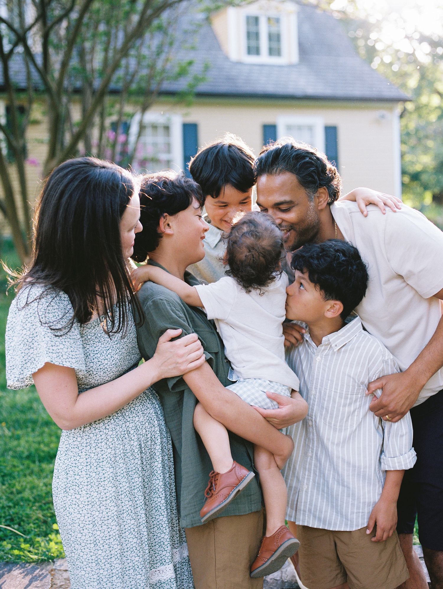 A family shares an intimate moment together outside their home on a sunny day, embracing and smiling with joy.