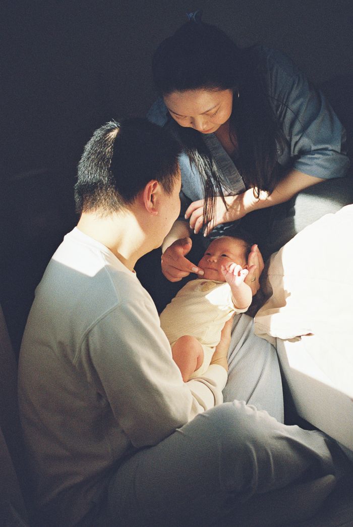 New parents lovingly looking at their sleeping newborn in dim light.