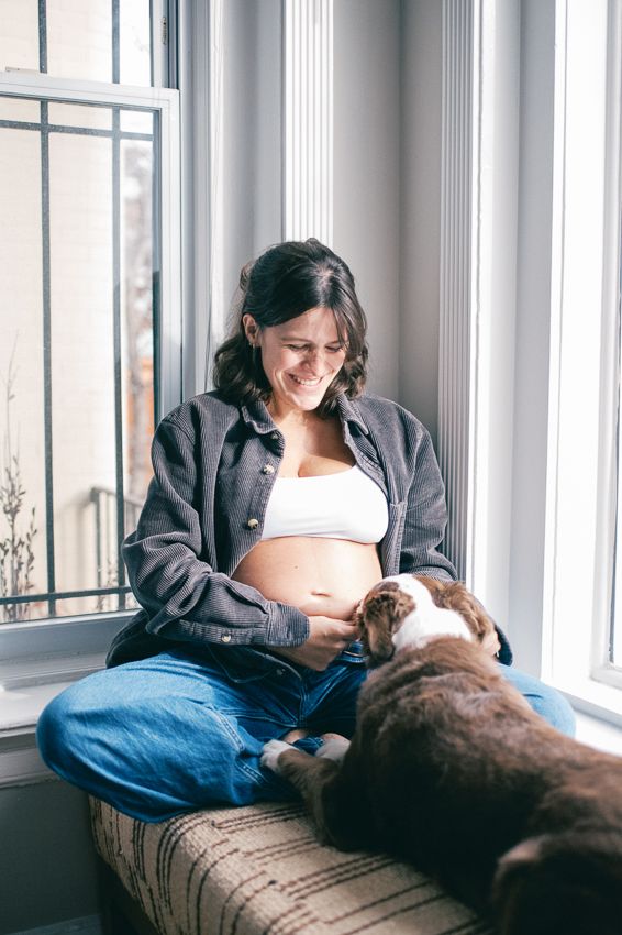 A person relaxes by a bright window with their dog on a cushioned windowsill.