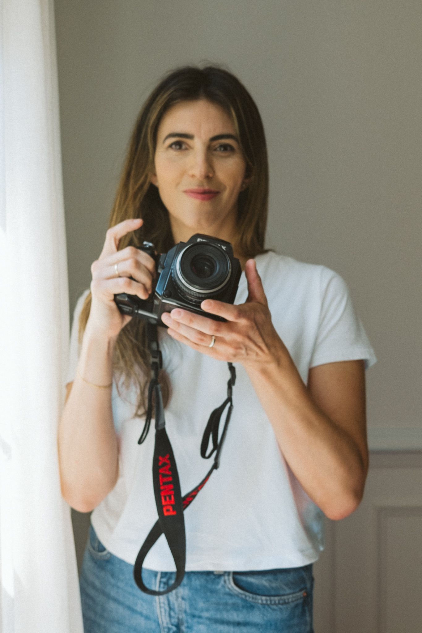 A photographer in a white t-shirt and jeans holds a camera in three similar self-portrait compositions.