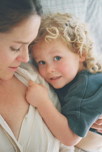 A mother tenderly looks down at her curly-haired toddler with blue eyes, sharing a warm, intimate moment together.