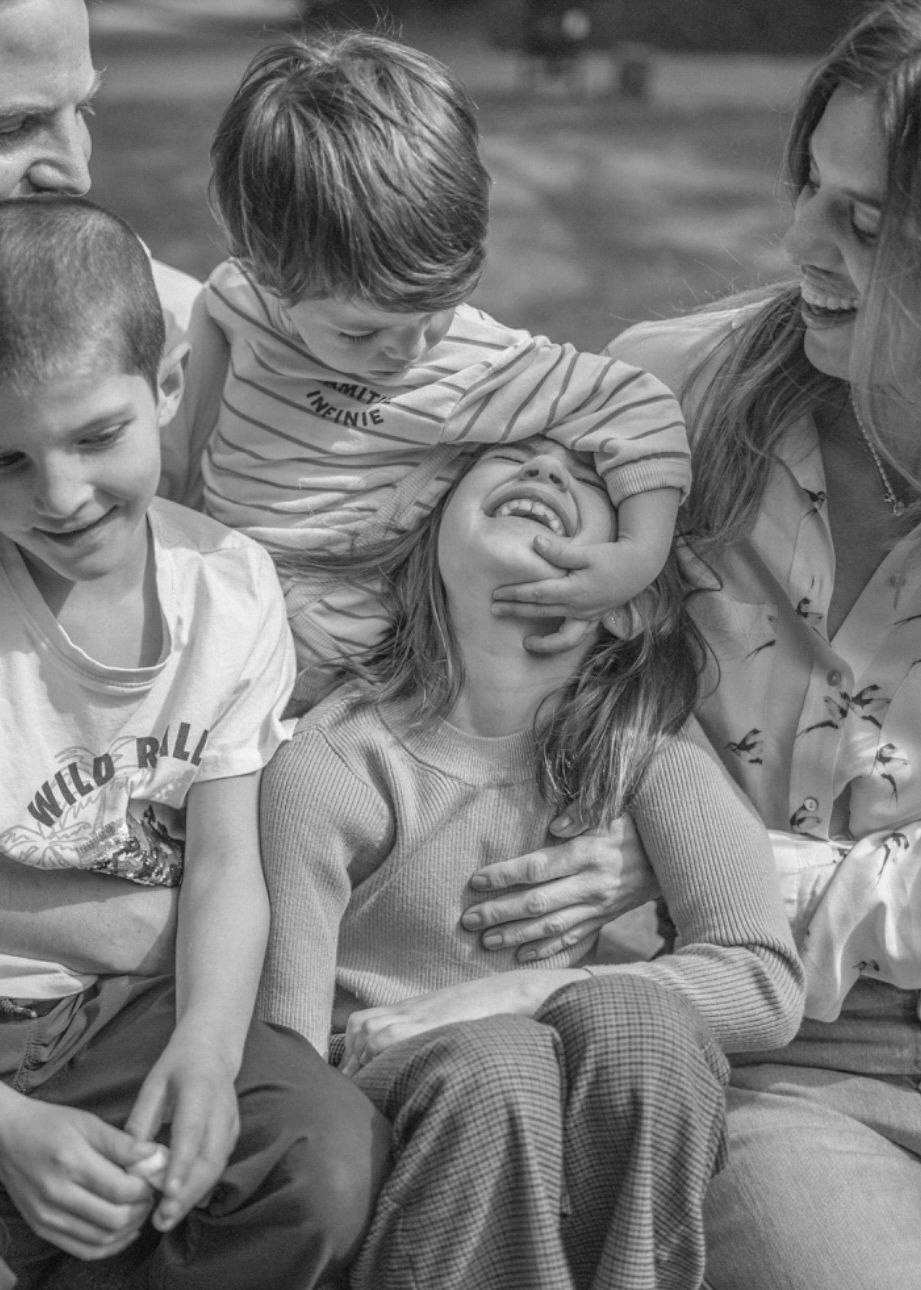 A black and white candid moment of a family laughing together while sitting outdoors.