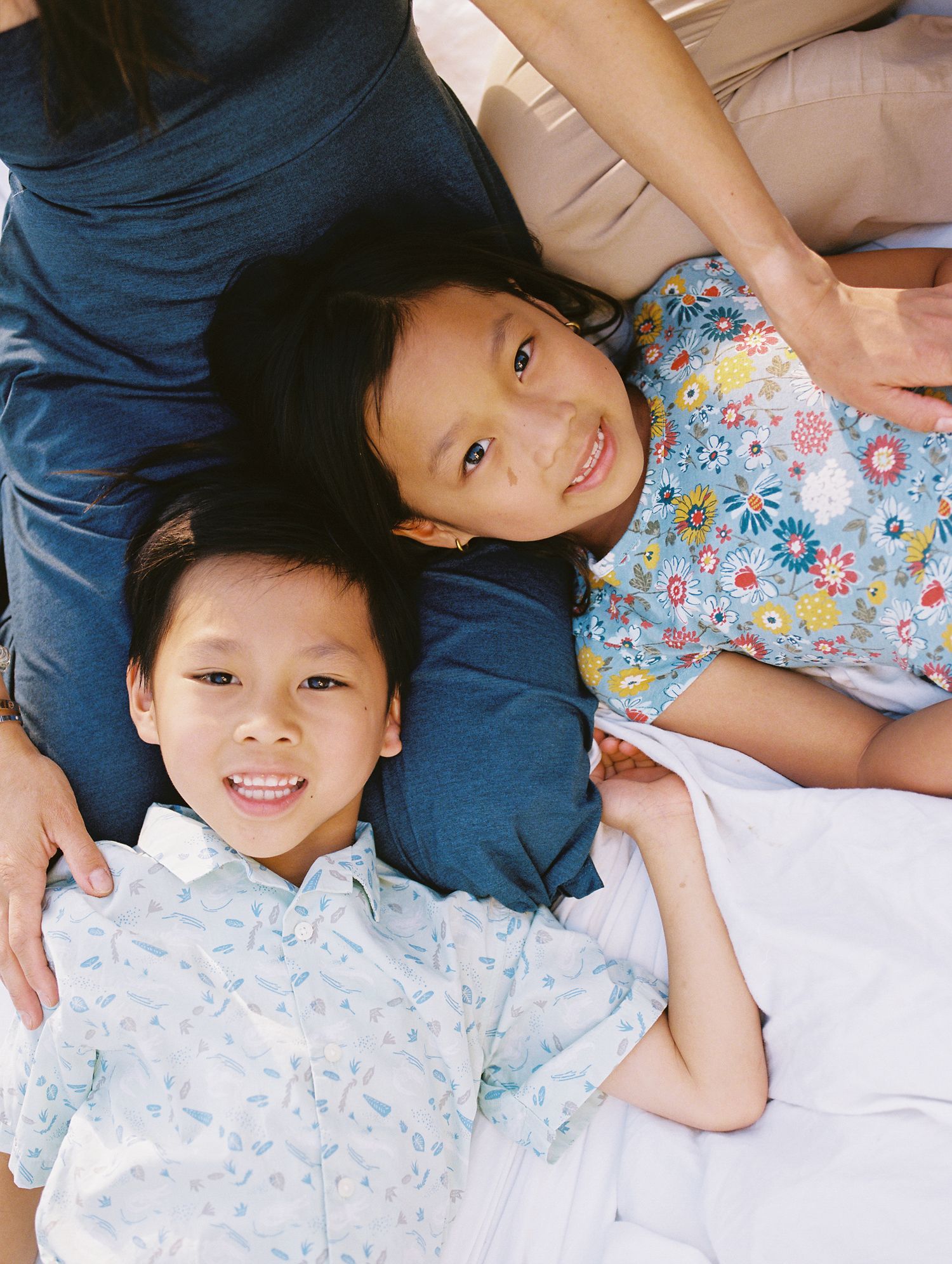 Two children laying together smiling at the camera, wearing floral and light colored clothing.