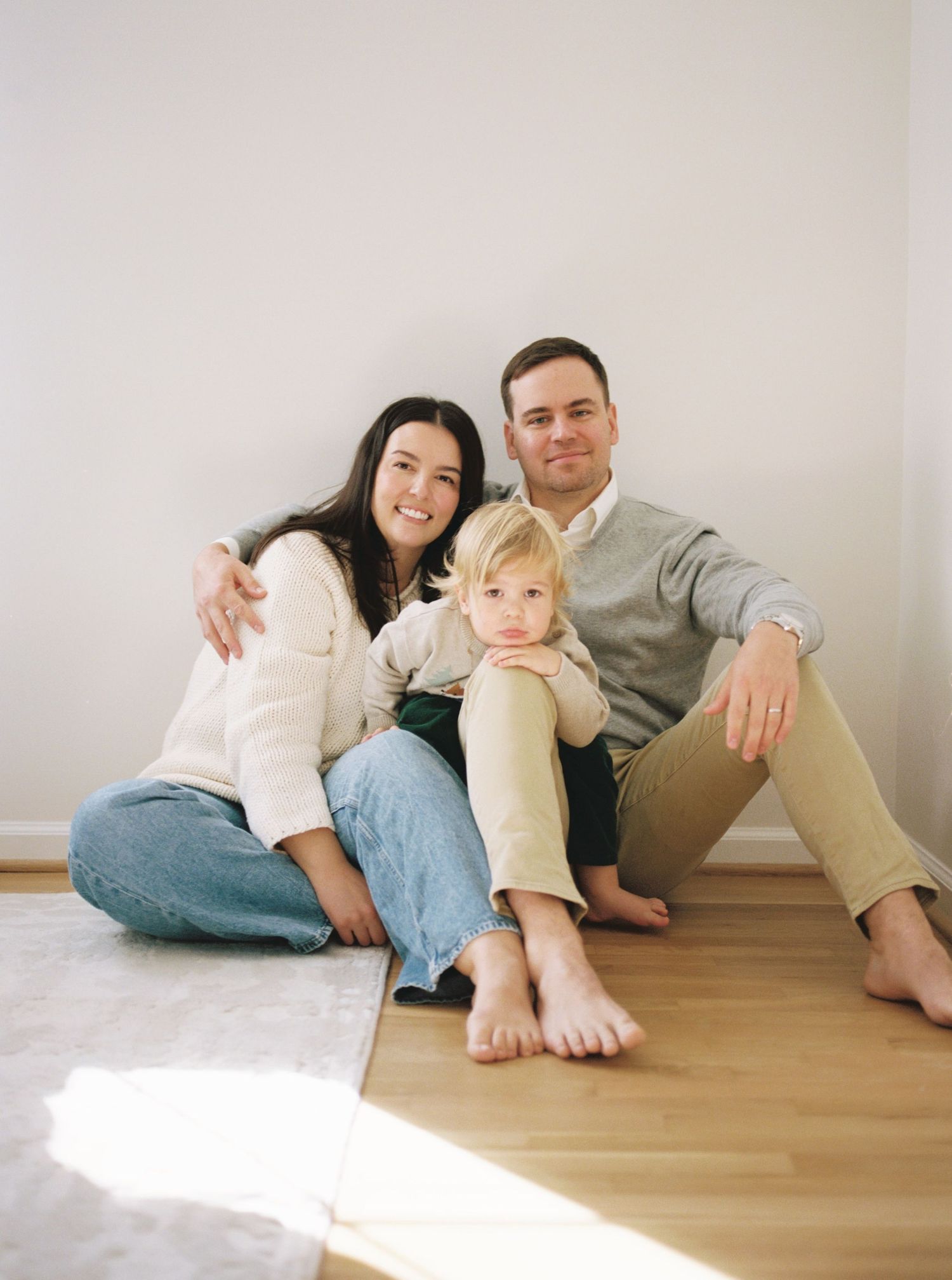 A family relaxes together on a hardwood floor in a bright, minimalist room.