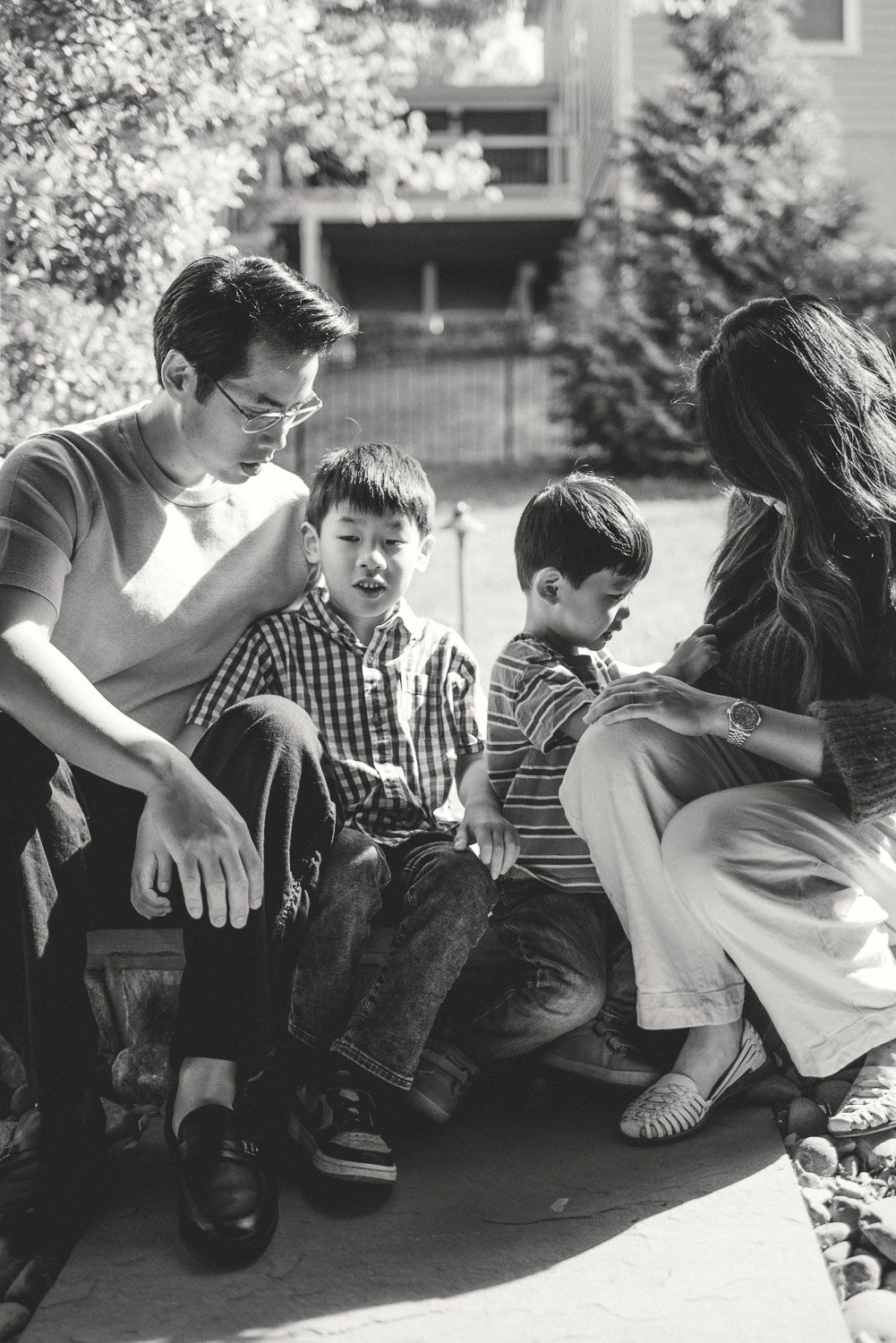 Black and white family portrait of parents and two young boys sitting together outdoors near a building.