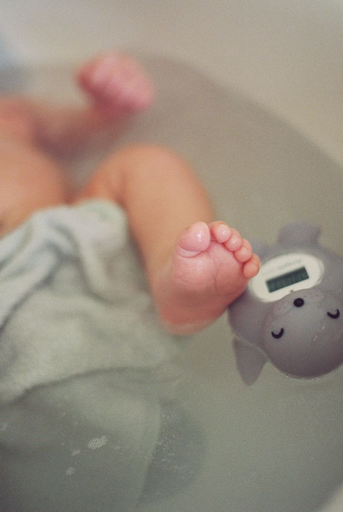 Baby feet resting on a hippo bath thermometer toy during a gentle infant bath time.